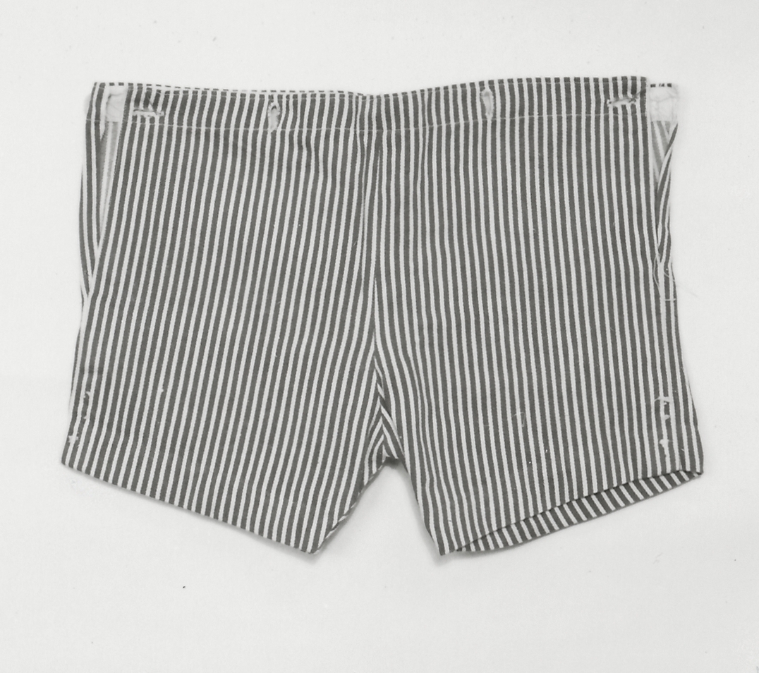 Barnkostym, av bomull, blå och vitrandig (Sjöman).
a) Jacka, utsvängd med skärp. Knäppning på höger sida. Lång ärm.
Mått: L 36cm bak.
b) Byxor, kort med knäppning i sidorna.
Mått: L 29cm.
c) Krage, blå med påsydda vita ränder.
Mått: Bredd 30cm.