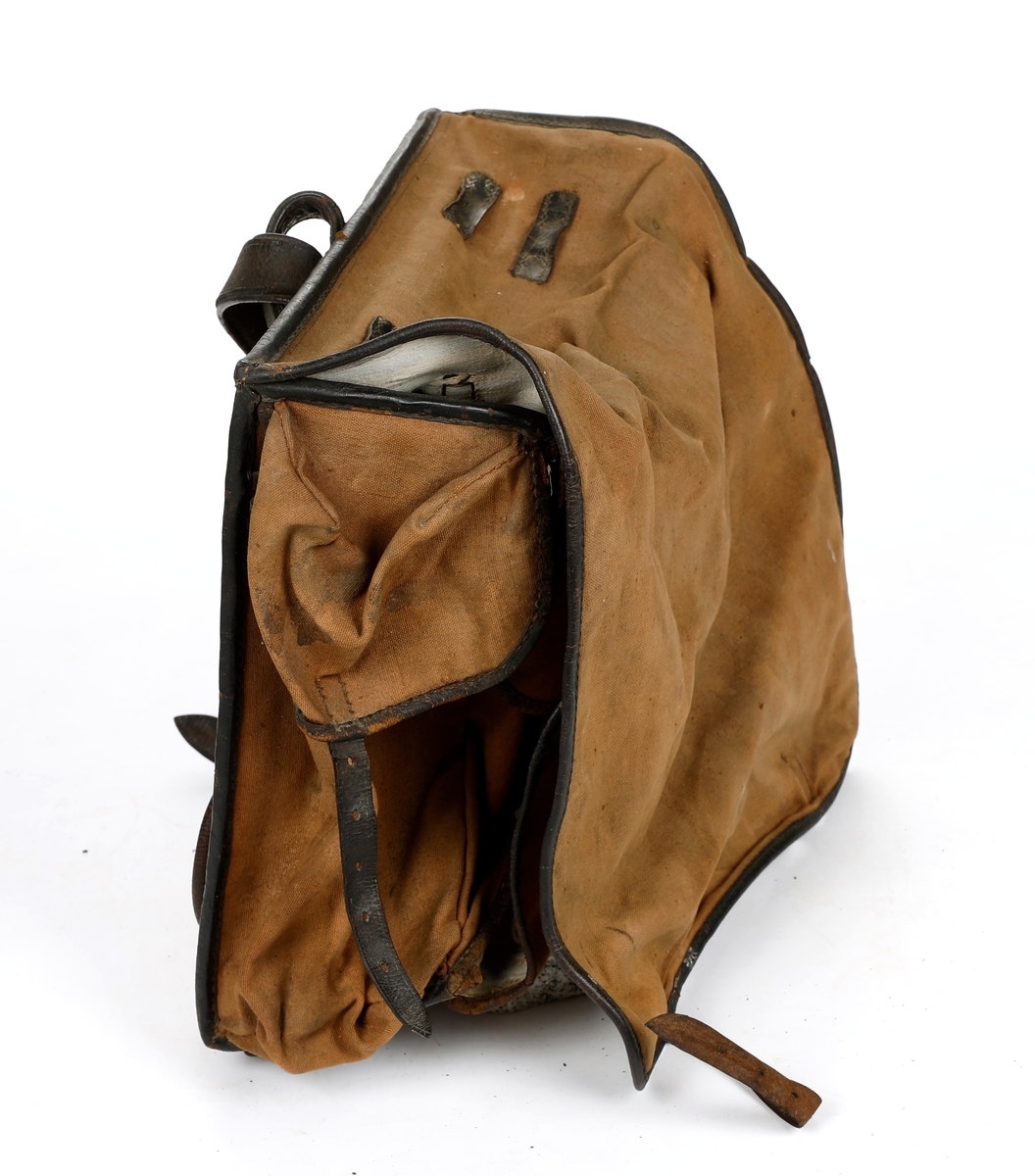 Militærransel i tekstil med kantet med lær. Lommer på hver side av ranselen. Foret med tekstil i bomull. Skulderreimer i læs, hvorav en kan festes til en metallspenne og den andre til en hekte. To doble smøystole på toppen av ranselen. Under lokket er det fire klaffer, to reimer i lær på ytre klaff og en reim på indre klaffer, som som festes til metallspenner. Ranselen er misformet.