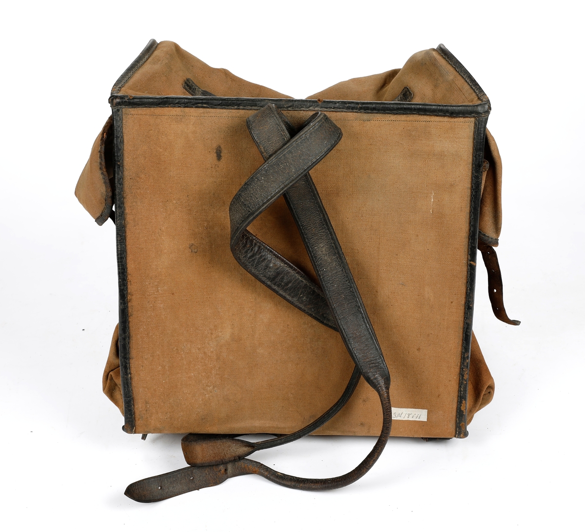 Militærransel i tekstil med kantet med lær. Lommer på hver side av ranselen. Foret med tekstil i bomull. Skulderreimer i læs, hvorav en kan festes til en metallspenne og den andre til en hekte. To doble smøystole på toppen av ranselen. Under lokket er det fire klaffer, to reimer i lær på ytre klaff og en reim på indre klaffer, som som festes til metallspenner. Ranselen er misformet.