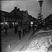 Ungdomar går i mörkret på Brahegatan. Tända julgranar på torgmuren till höger. Det ligger lite snö på marken.