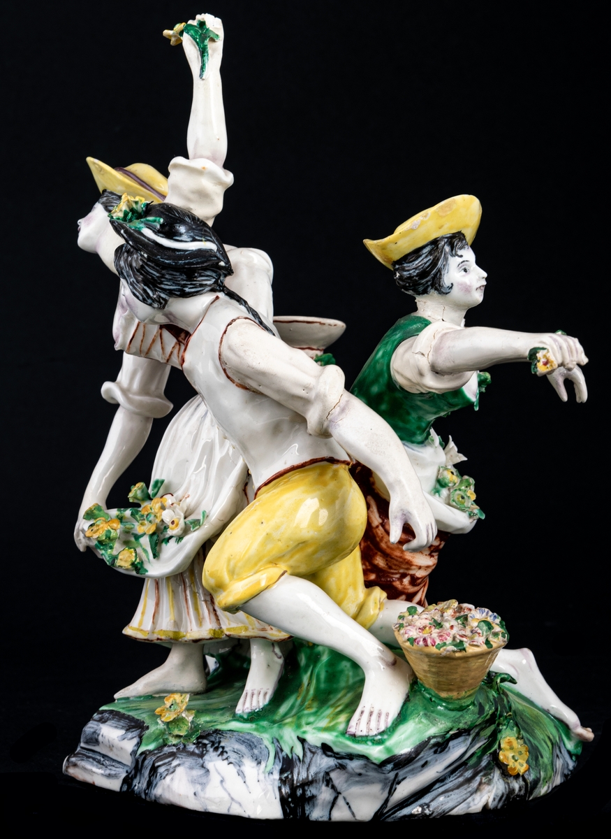 Figurgrupp. Herde och blomsterplockerskor, grupp av mjukt porslin.
Märke: MB - Marieberg. Berthevins tid 1766-1769, oläsligt, H. F. (tillverkad av Hierner?)

Gruppen består av en mansfigur och två kvinnofigurer samt en urna på en trädstam. Målat i polykromoa färger - grönt, brunt och gult.