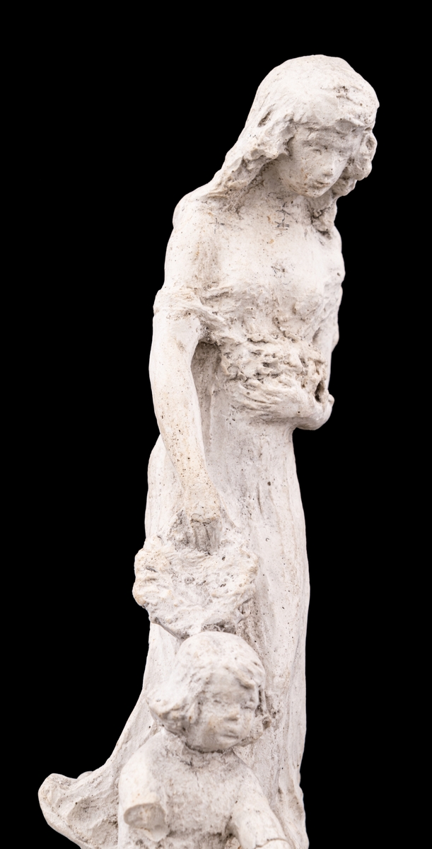 Skulpturskiss av Ida Matton, signerad Paris 1920, till gravmonument för redarfamiljen Brodin i Gävle. Kvinna med blommor i händerna med ett barn med blomgirlang sittande framför fötterna. Båda placerade på en trekantig sockel som liknar stäven på en båt.