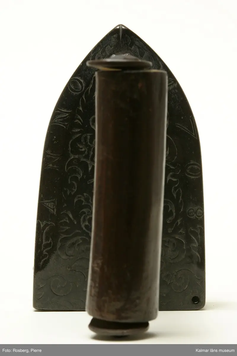 KLM 5925. Strykjärn. Av malm. Järnet framtill spetsigt. Handtag av trä. Lodet och luckan saknas. Övre ytan prydd med gjuten reliefornering i form av rankor samt ANNO 1708 .