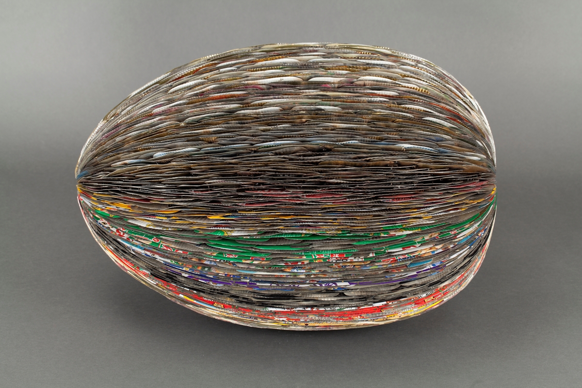 Eggformet skulptur, satt sammen av utallige tilskårede metallplater fra hermetikkbokser. Metallplatene er festet lag på lag rundt en akse og kan minne om formen til en kongle.