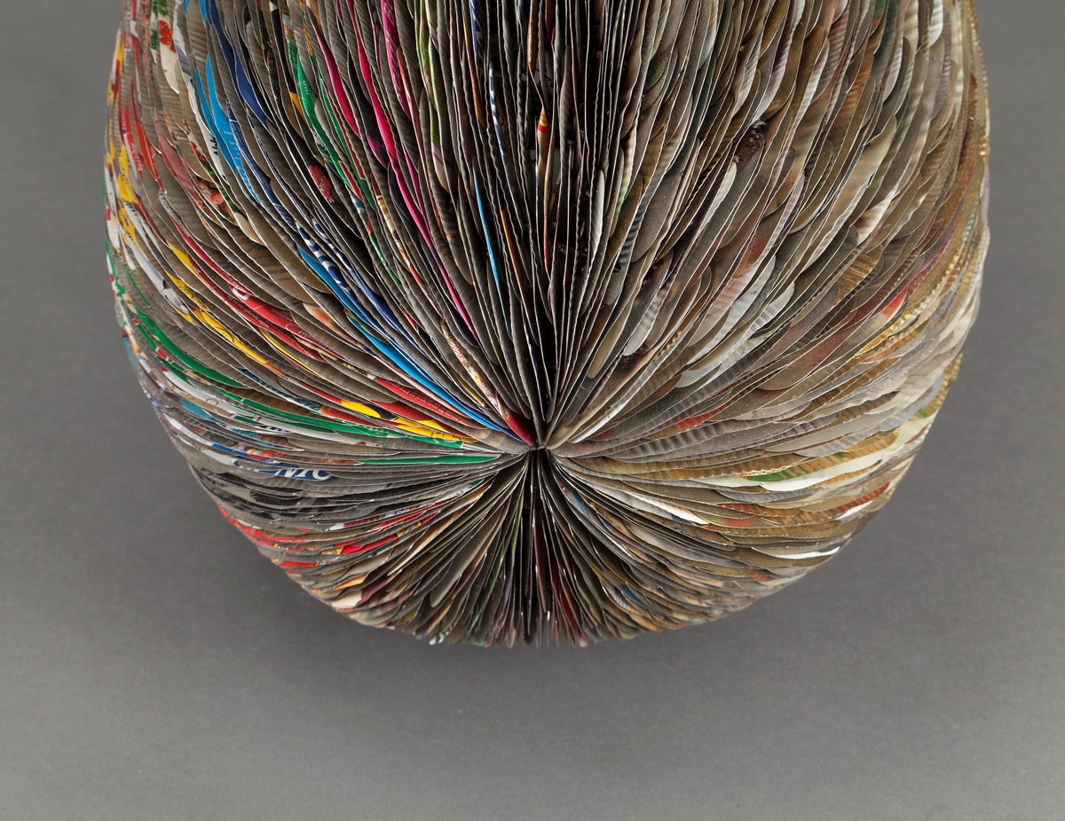 Eggformet skulptur, satt sammen av utallige tilskårede metallplater fra hermetikkbokser. Metallplatene er festet lag på lag rundt en akse og kan minne om formen til en kongle.