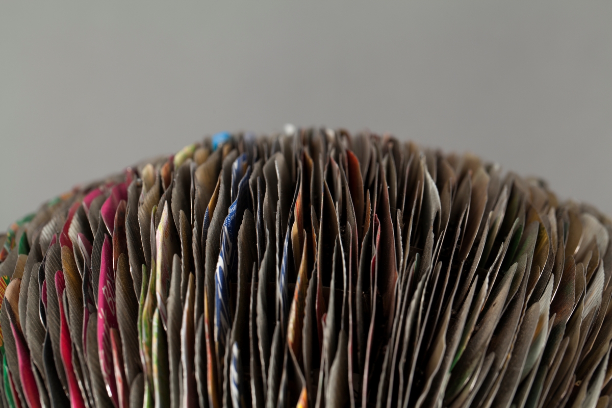 Eggformet skulptur, satt sammen av utallige tilskårede metallplater fra hermetikkbokser. Metallplatene er festet lag på lag rundt en akse og kan minne om formen til en kongle.