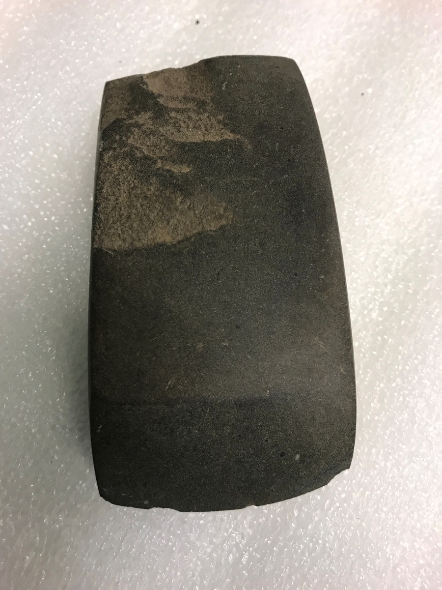 Rektangulær, tverregget øks av grågrønn, tett, finkornet bergart, av typen [Rygh fig.13]R. 13, men med rett nakke. Noen arr etter tilhugningen sitter igjen, ellers omhyggelig slipt og godt bevart. 