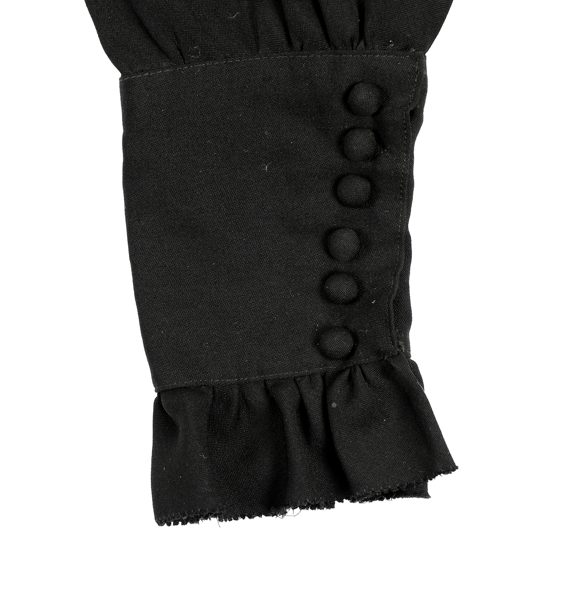 Helforet med svart mugg, 10 fine legg på forstykke som er løst. Bryststykke og halslinning har foldelagt chiffon. Øverst på halslinning rynkekappe av chiffon og smal hvit bobinetteblonde. Brodert chiffonlengde fra halsen og ut over skuldra. Svart blonde ut på skuldrene og på ned i en spiss V foran. Belte i livet. Kappe på hver side under beltet med volang. Kappene fortsetter ned i to snipper bak. Mansjettene på hver erme er høye og lukkes med trykknapper med pynteknapper over.
 