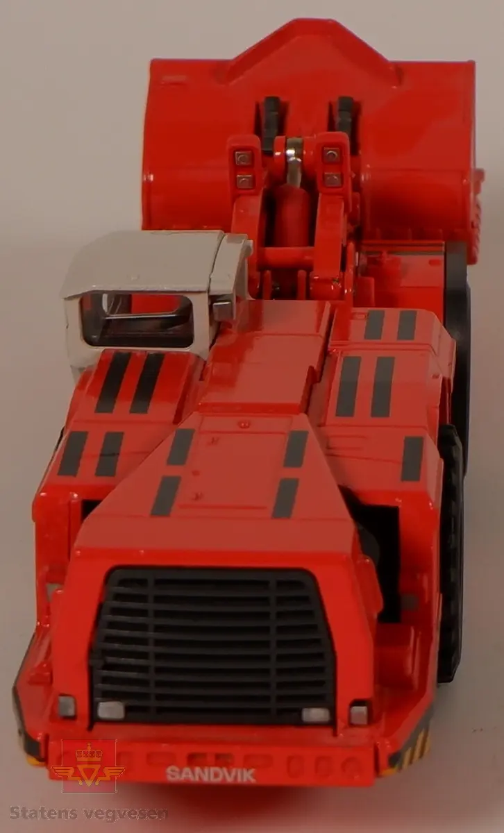 Sandvik LH621. Miniatyrmodell av en lastemaskin. Maskinen er produsert i metall med hjul av plast som er påsatt gummidekk. Modellen er rød med hvit hytte og har påskriftene SANDVIK og LH621. Innskriften conrad Made in Germany Scale 1:50 er preget inn i metallet på undersiden av maskinen.