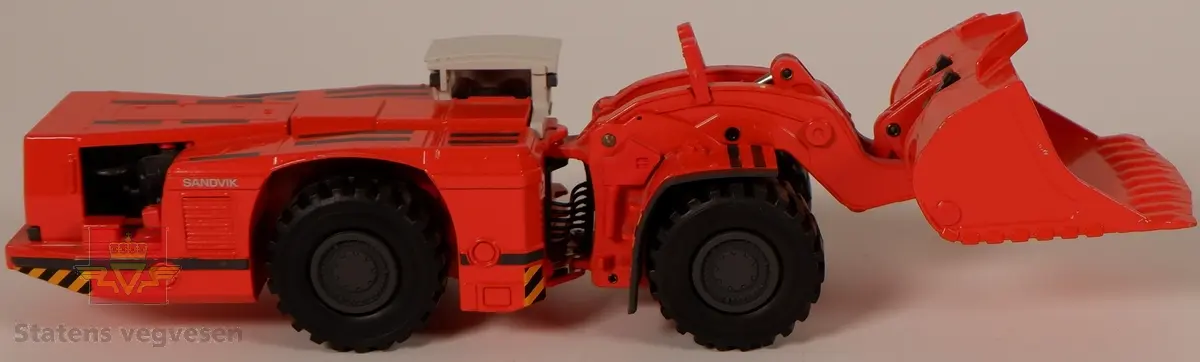 Sandvik LH621. Miniatyrmodell av en lastemaskin. Maskinen er produsert i metall med hjul av plast som er påsatt gummidekk. Modellen er rød med hvit hytte og har påskriftene SANDVIK og LH621. Innskriften conrad Made in Germany Scale 1:50 er preget inn i metallet på undersiden av maskinen.