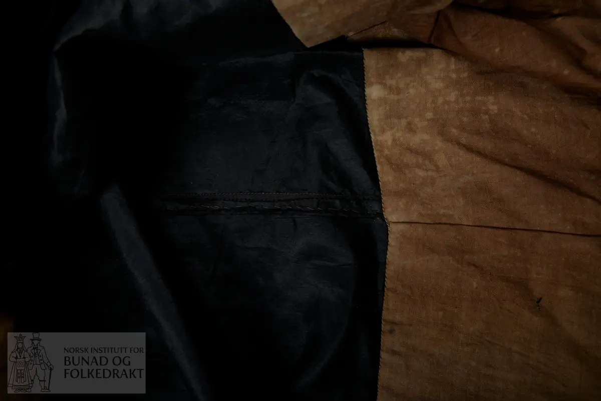 Brudeskjørt i svart silketaft, trolig brukt sammen med understakk NBF2021-0840.
Mørk grønt kypertvevd bånd påsydd for hånd rundt nedkant. 
Bomullsstoff , lerret til skoning.
Piperynket bak.
Splitt litt mot venstre side bak.