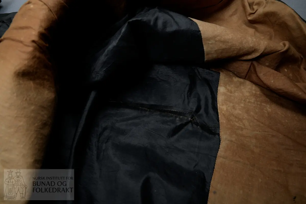 Brudeskjørt i svart silketaft, trolig brukt sammen med understakk NBF2021-0840.
Mørk grønt kypertvevd bånd påsydd for hånd rundt nedkant. 
Bomullsstoff , lerret til skoning.
Piperynket bak.
Splitt litt mot venstre side bak.