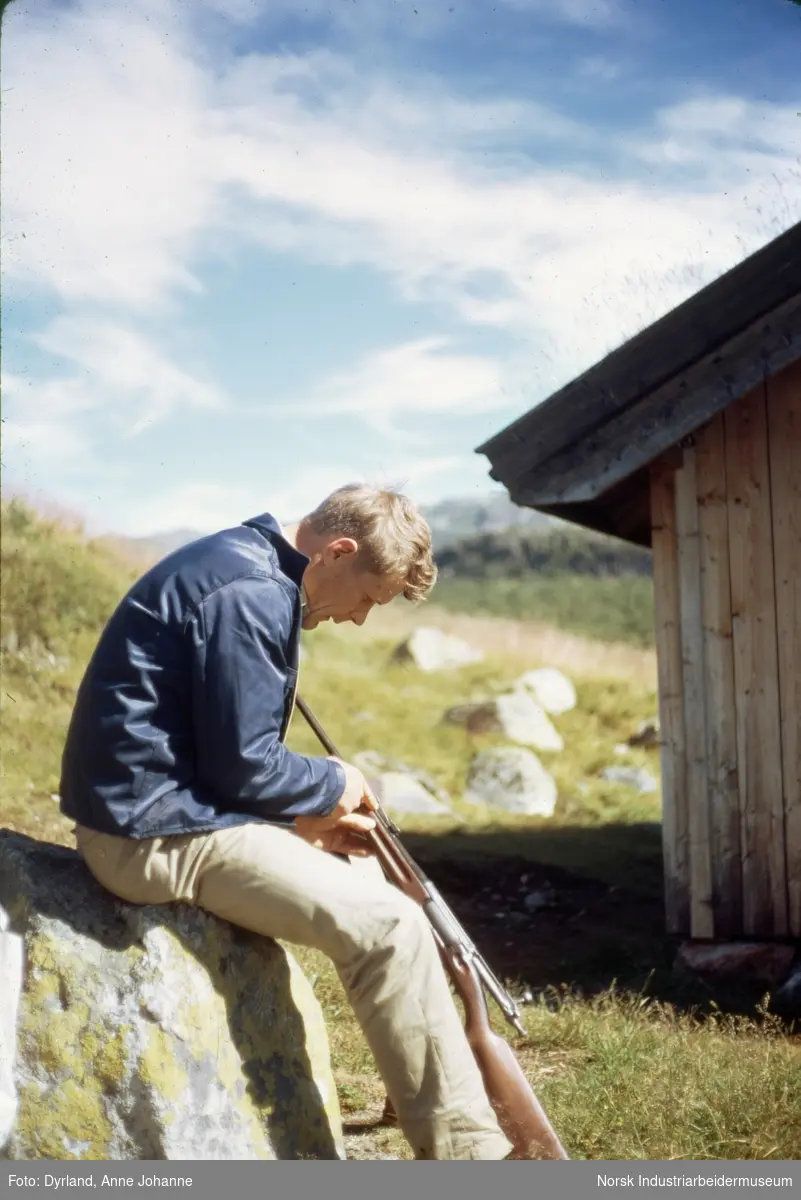 Bjørn Dyrland renser et gevær mellom bena mens sitter på en sten utenfor hytte på Dalastaul i Åmotsdal