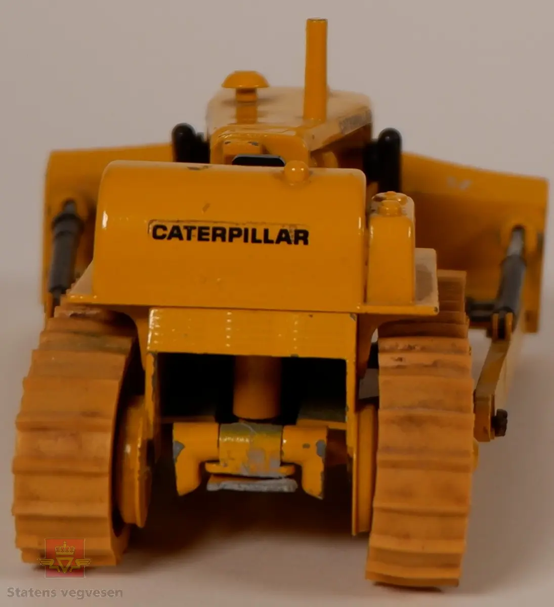 Caterpillar D9G. Leketøy, miniatyrbulldozer av metall og gummi. Gul med enkelte svarte detaljer. Dozeren går på belter og har skjær foran. Merking fra produsenten under leketøyet samt Caterpillar merking utenpå.