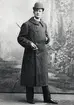 En man i vinterrock och hatt m.m. poserar för fotografen.
Helfigur, ateljéfoto, ca 1890.