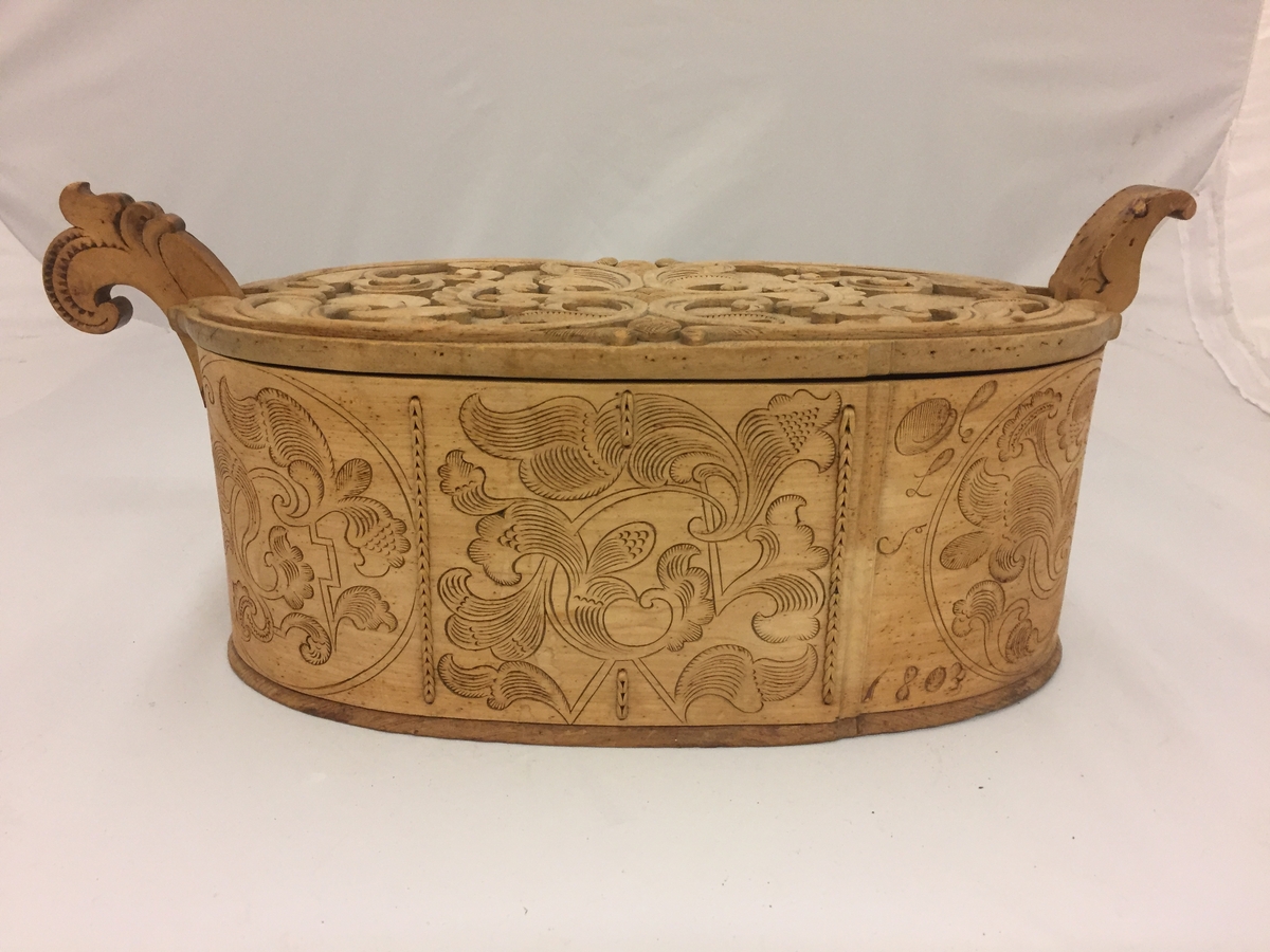 Sveipa, oval tine med utskjeringar. Flat, innrissa skurd på sjølve asken. Loket har også utskjeringar. C-krullar, blad, sirkelformer m.m. Bokstavane  (?) L S 1803 er skore inn. Eit "øyre" på kvar side av tina.