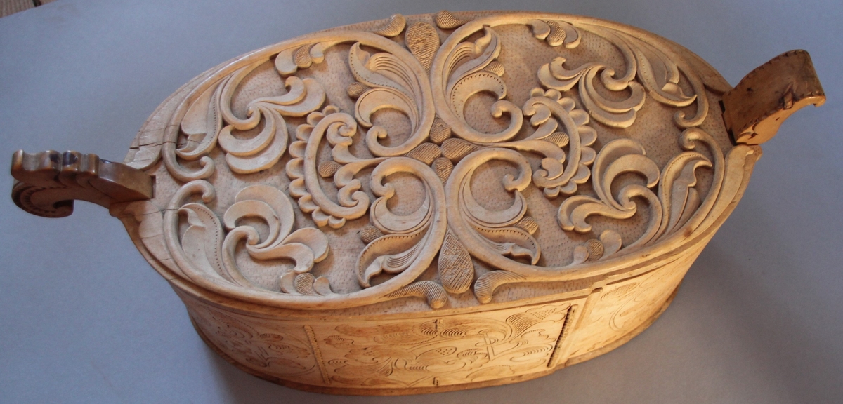 Sveipa, oval tine med utskjeringar. Flat, innrissa skurd på sjølve asken. Loket har også utskjeringar. C-krullar, blad, sirkelformer m.m. Bokstavane  (?) L S 1803 er skore inn. Eit "øyre" på kvar side av tina.