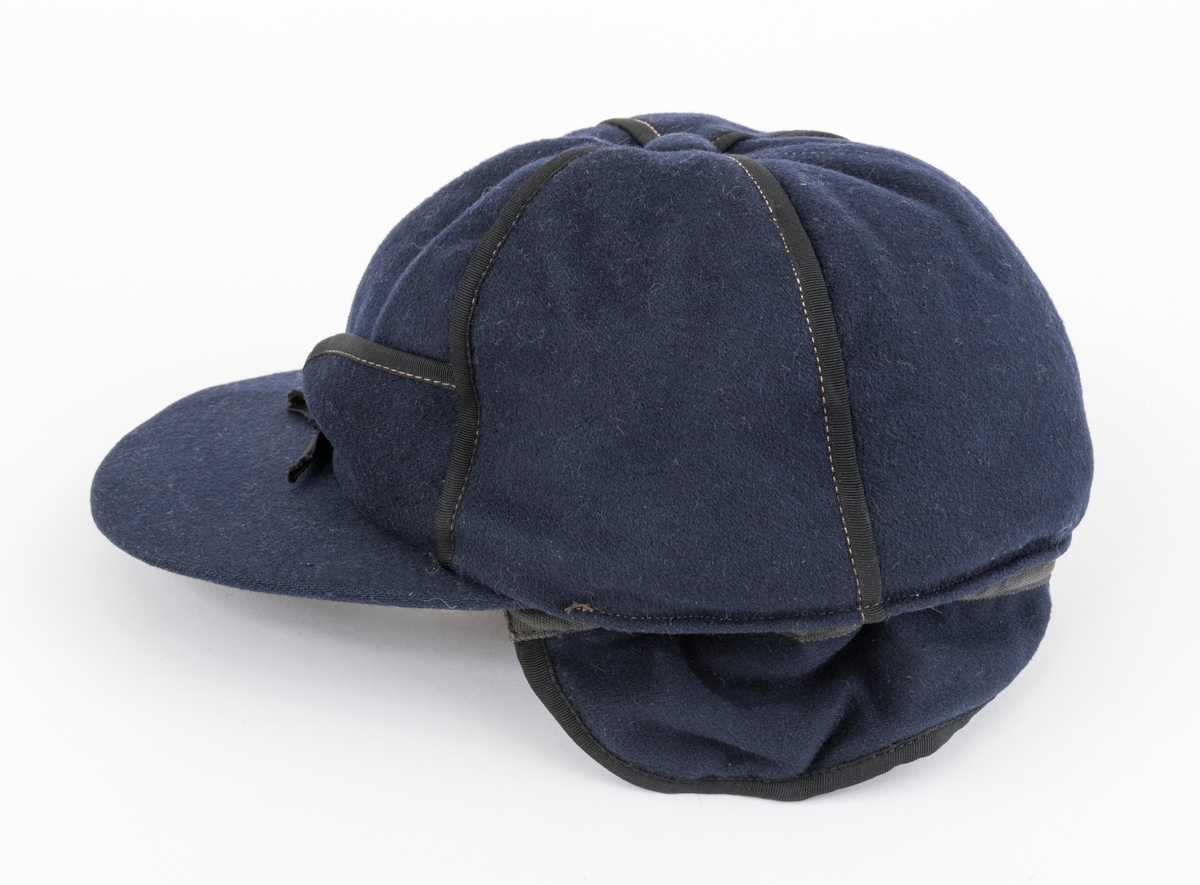 Lua er ei østerdalslue av den modellen som Olai Pedersen lanserte i 1906.  Den er sydd av mørkeblå vadmel og kantete med svart stoff.  På innsida av øreklaffene er det brunt skinn. 