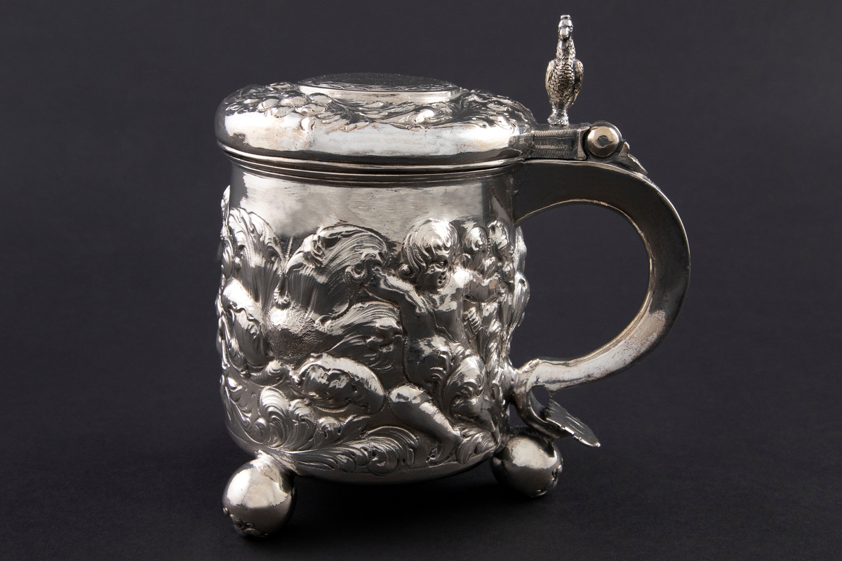 Drikkekanne i sølv med sylinderformet korpus, hank og hengslet lokk. Kannen står på tre kuleføtter dekorert med hver sin blomst. Korpus er dekorert med drevet blomsterdekor blant tre kjeruber. Lokket har en krans med drevet blomster- og akantusranke med fugler. I sentrum er en sirkel med initialer inni en laurbærkrans. Lokkåpner er formet som en hane. Hanken er dekorert med akantusranke som ender i en blomst.