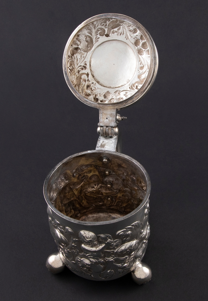 Drikkekanne i sølv med sylinderformet korpus, hank og hengslet lokk. Kannen står på tre kuleføtter dekorert med hver sin blomst. Korpus er dekorert med drevet blomsterdekor blant tre kjeruber. Lokket har en krans med drevet blomster- og akantusranke med fugler. I sentrum er en sirkel med initialer inni en laurbærkrans. Lokkåpner er formet som en hane. Hanken er dekorert med akantusranke som ender i en blomst.