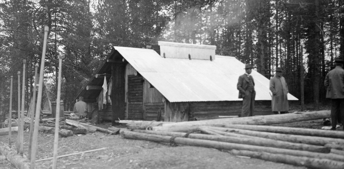 Tverenbrakka ved Osensjøen.  Dette var ei lav, men stor tømmerkoie.  Det var bare fire-fem omfar opp til raftstokken, og røstet var innkledd med vertikal glattpanel (låvepanel).  Inngangsdøra var plassert midt på gavlveggen, og taket var noe utkraget over døra..  Da dette fotografiet ble tatt ser det ut til at taket var tekket med bølgeblikk.  Ved mønet er det slått opp lemmer, slik at det er dannet en ljore hvor røyken fra langåren inne i koierommet stiger opp. Ved siden av inngangsdøra er det opphengt en del klær, og ved siden av sitter en fløter.  I forgrunnen står tre karer, hvorav en er iført dress og hatt, en annen frakk og hatt ved noe som later til å være lensestokker.  I forgrunnen til venstre er en del fløterhaker «parkert» ved å hogge stingar'n ned i en stokk som ligger på standa.