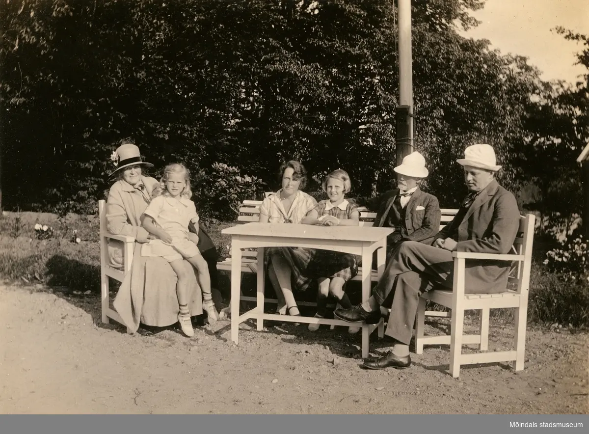 Från vänster ses Bibbi Björck sittandes i knät på en dam, på bänken Laila Björck med dottern Ulla samt även Lailas far.

Fotografi taget i juni 1929 vid sommarbostaden Strandlyckan vid Landvettersjön, Slamby 1:4 i Landvetter socken. Huset övertogs senare av Stiftelsen Enandergården, Härlanda församling, på 1950-talet.