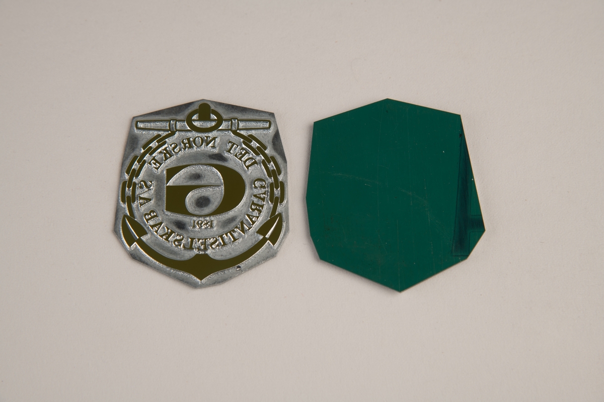 En metallplate med uthevet logo. En stilisert G i en sirkel av skrift, omkranset av kjetting og et anker.