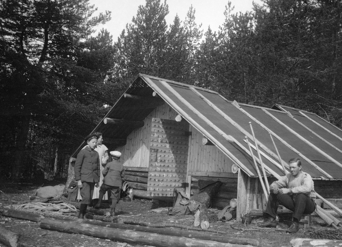 Fløterbrakka ved Tverrenhullet ved Osensjøen.  Brakka er forholdsvis lav, men likevel stor.  Det er bare fire-fem laftete omfar opp til jamnveggen (raftet).  I røstet er det vertikalstilt glattpanel.  Her er inngangsdøra plassert.  Taket later til å være tekket med jernplater, antakelig fra oppklipte fat (tønner).  Skjøtene mellom platene er dekt av påspikrete bord.  I mønet er det en forholdsvis lang ljoreåpning.  Brakka skal ha hatt langåre langs rommets midtakse og brede liggebrisker langs begge langveggen.  Her kunne det ligge opptil 20-30 mann.  Da fotografiet ble tatt satt en kar ved hjørnet av koia.  Bak ham stod det tre fløterhaker med skaftene mot takskjegget.  Foran inngangsdøra sto ei kvinne og to gutter. 