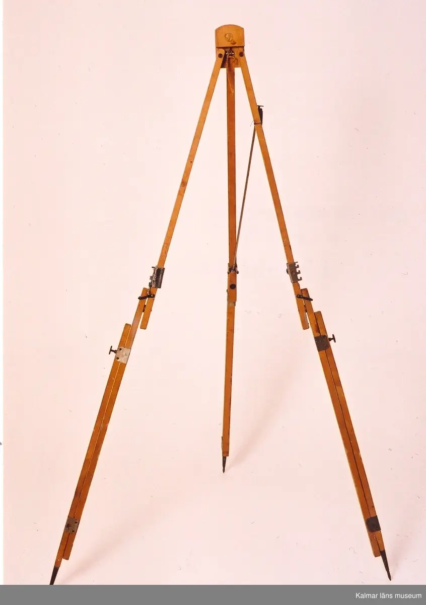 KLM 31955. Staffli av trä. Hopfällbart stativ på tre ben. Reglerbar höjd. Skjutbara tavelstöd på benen. Staffliet har överst ett påklistrat runt märke med en grön fågel och texten ASP. Skrivet med blyerts på staffliet: 22:- (sannolikt priset).