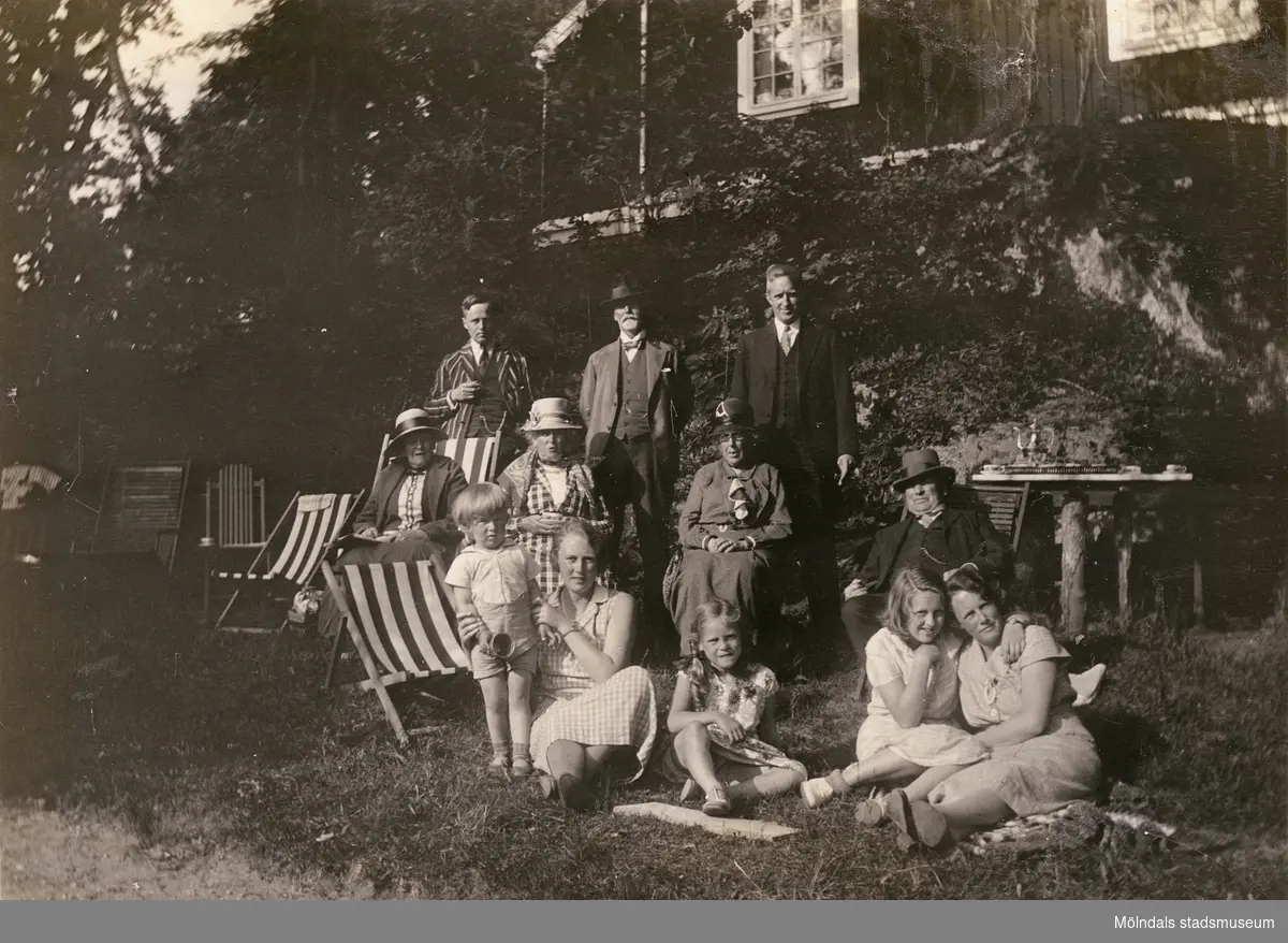 Sommarbild med hela släkten uppställda för ett grupporträtt i trädgården.

Fotografi taget i juni 1932 vid sommarbostaden Strandlyckan vid Landvettersjön, Slamby 1:4 i Landvetter socken. Huset övertogs senare av Stiftelsen Enandergården, Härlanda församling, på 1950-talet.