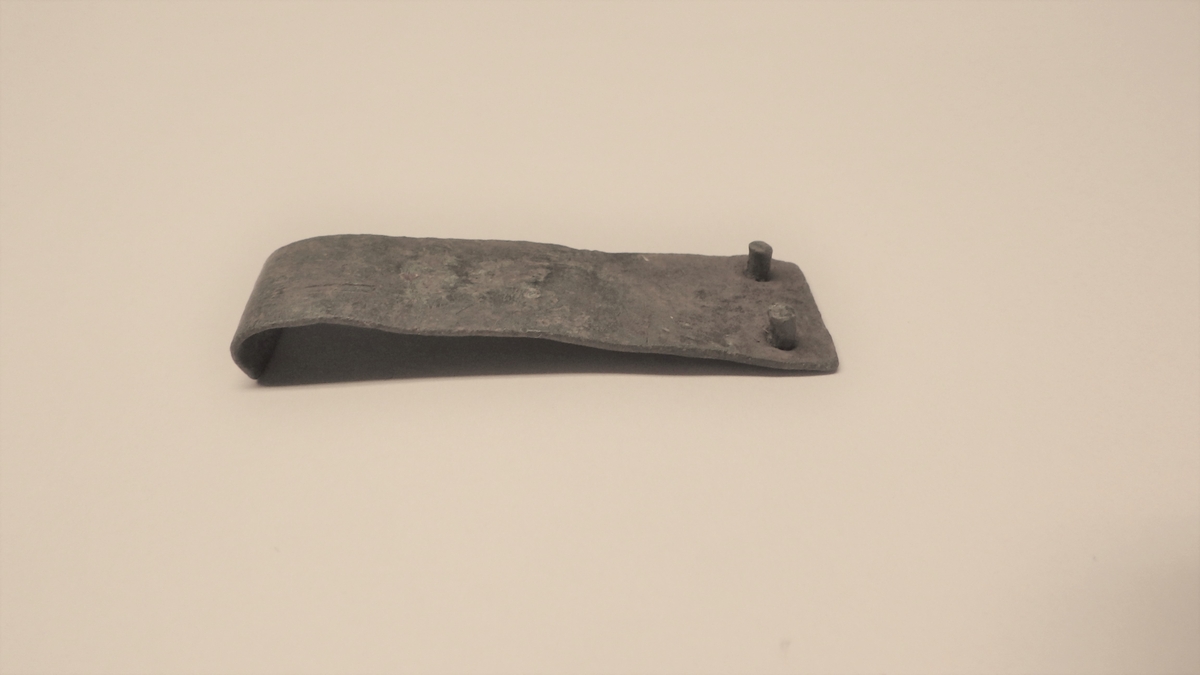 MALV: L. 46 MM B. 15 MM, SVAKT TRAPESFORMET PLATE MED TO NAGLER I DEN BREDESTEENDEN, OMBØYD I DEN SMALESTE ENDEN. 