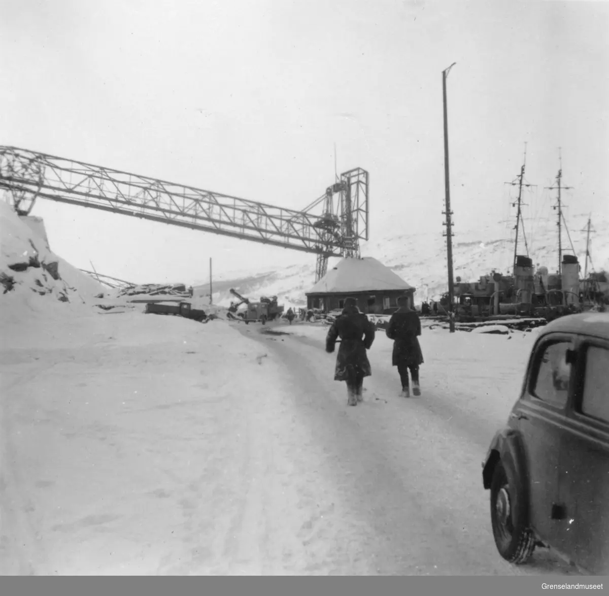 To menn går mot malmkaia- østre bro. Et skip ligger til kai. Kirkenes vinteren 1944/45.