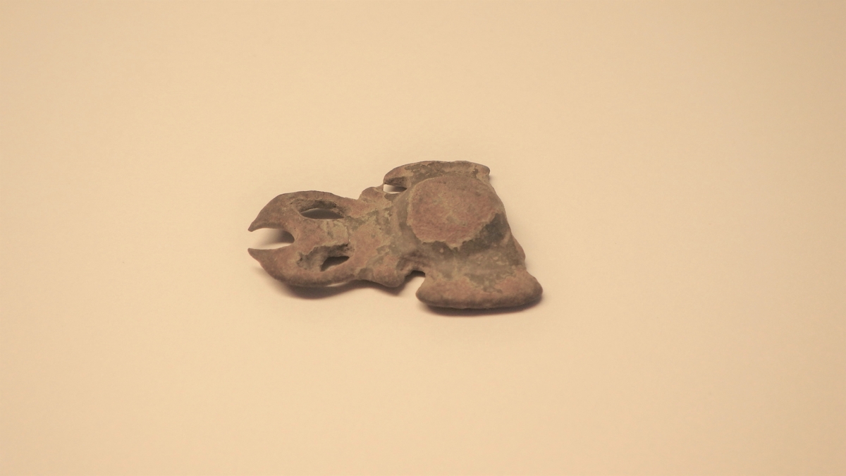 MALV: L. 2, 6 CM, B. 2, 1 CM, STØPT, AVBRUKKET. BUKLE PÅ MIDTEN, HAR VÆRT SYMETRISKOMKRING DENNE. GJENNOMBRUTT. 