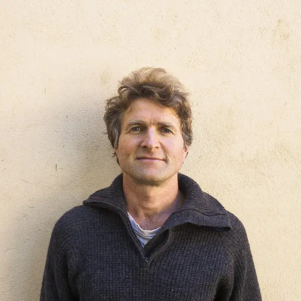 Mann i mørk ullgenser foran lys murvegg