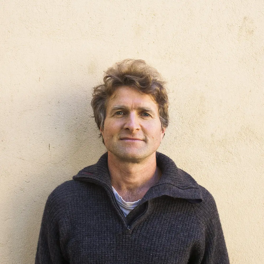 Mann i mørk ullgenser foran lys murvegg