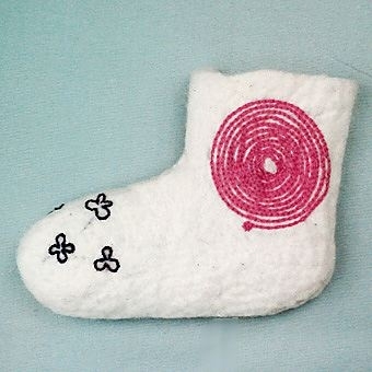 Socka tovad av naturvit ull, troligtvis gobelinull. Sockan har en naturligt avslutad rak kant. Broderi på skaftets utsida med rosa tvåtrådigt ullgarn i form av en spiral i kedjesöm. På sockans spets är broderat lila blommor i stjälksöm. Vänstersocka.