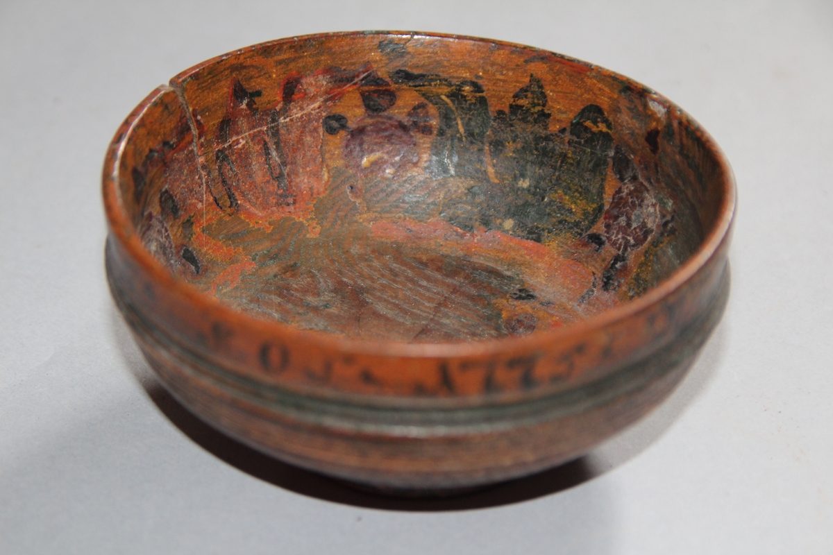 Liten dreia bolle. Rosemåla med tekst kring kanten på utsida. Teksten er utydleg men det kan lesast "R.O.S.1775 sett(?) nu mig bie(?) snart får du rusen føle" Rosemåling inni bollen, blad og blomstermotiv. Rosemålinga er noko slitt. Utanpå er bollen brunmåla, med ei grøn stripe og orange kant. Bollen har ein skade på den eine sida. denne skaden er lima.