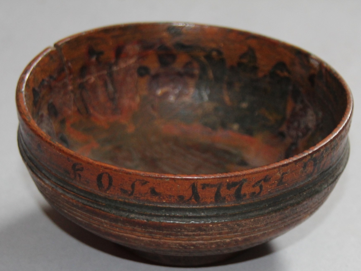 Liten dreia bolle. Rosemåla med tekst kring kanten på utsida. Teksten er utydleg men det kan lesast "R.O.S.1775 sett(?) nu mig bie(?) snart får du rusen føle" Rosemåling inni bollen, blad og blomstermotiv. Rosemålinga er noko slitt. Utanpå er bollen brunmåla, med ei grøn stripe og orange kant. Bollen har ein skade på den eine sida. denne skaden er lima.