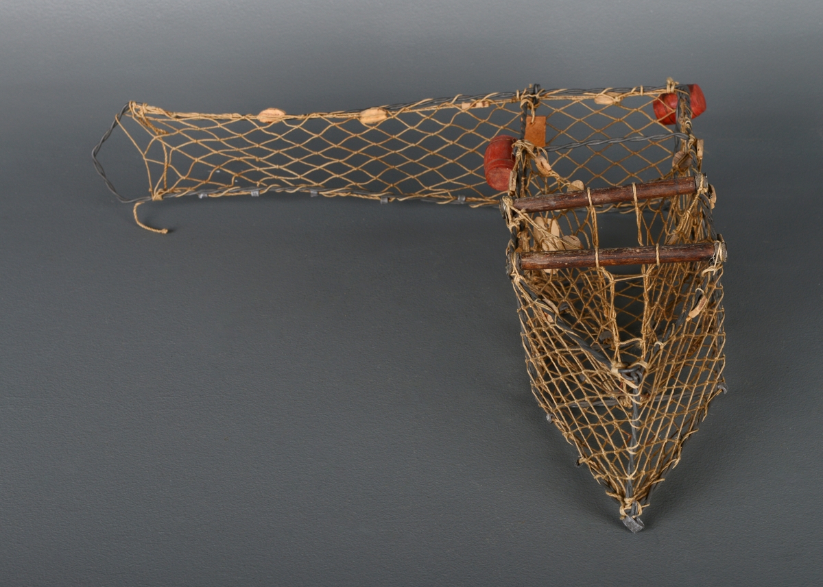 En modell av en kilenot med metallskjelett og nett. Laget av ståltråd, hyssing og kork. Den er montert og skrudd og tvinnet sammen. Viser hvordan redskapet fungerer for å fange laks.
