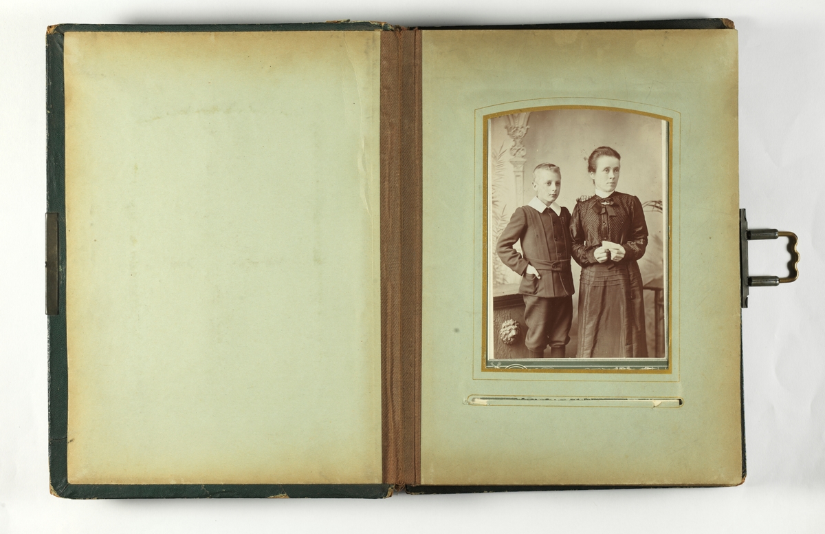 Svarthvitt-fotos i album med mørkegrønn skinnimitert perm og metallspenne.