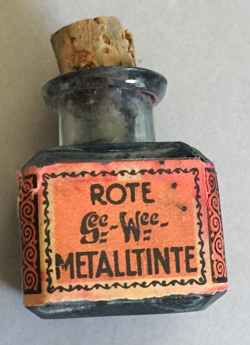 Lite blekkhus med kork. Korken er knekt, Sjølve blekkhuset er i glas og har raud etikett med teksten"Gunter wagner Hannover und Wien Rote Metalltinte Schutzmarks Pelikan"