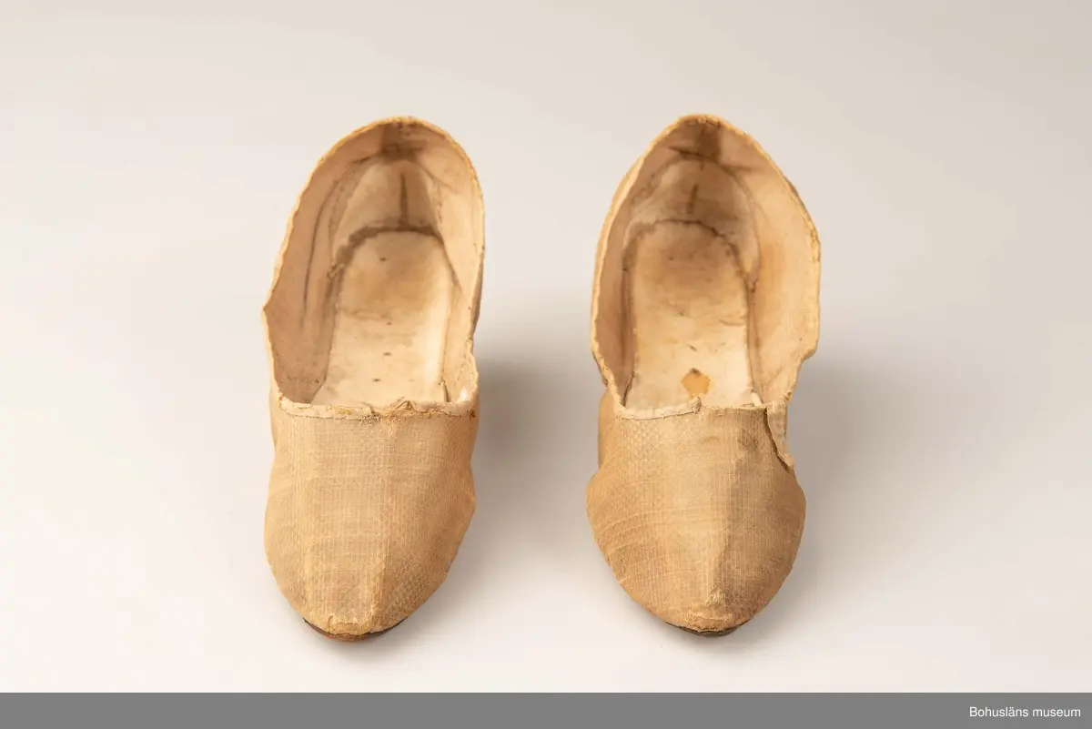 Ur handskrivna katalogen 1957-1958:
Fruntimmersskor
Sulornas L. c:a 23 cm. Chagrinerat siden, gult. Sulor av läder, innersulor o klack; av vitt skinn. Tyget nt trasigt. Troligen fr 1700-talet. Bohuslän

Antecknat i Gåvobok 1875, december: Fru Gottfrida Wesslau. Ett par skor från förra århundradet.
