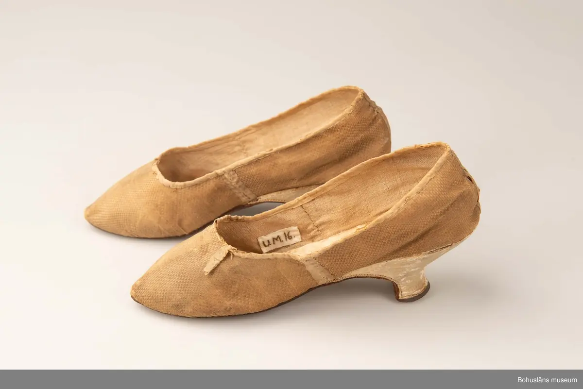 Ur handskrivna katalogen 1957-1958:
Fruntimmersskor
Sulornas L. c:a 23 cm. Chagrinerat siden, gult. Sulor av läder, innersulor o klack; av vitt skinn. Tyget nt trasigt. Troligen fr 1700-talet. Bohuslän

Antecknat i Gåvobok 1875, december: Fru Gottfrida Wesslau. Ett par skor från förra århundradet.
