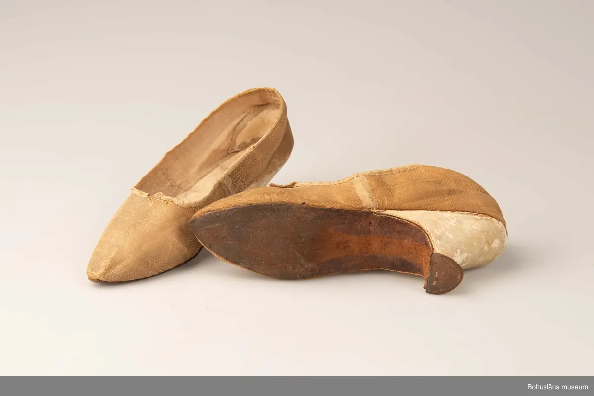 Ur handskrivna katalogen 1957-1958:
Fruntimmersskor
Sulornas L. c:a 23 cm. Chagrinerat siden, gult. Sulor av läder, innersulor o klack; av vitt skinn. Tyget nt trasigt. Troligen fr 1700-talet. Bohuslän

Antecknat i Gåvobok 1875, december: Fru Gottfrida Wesslau. Ett par skor från förra århundradet.