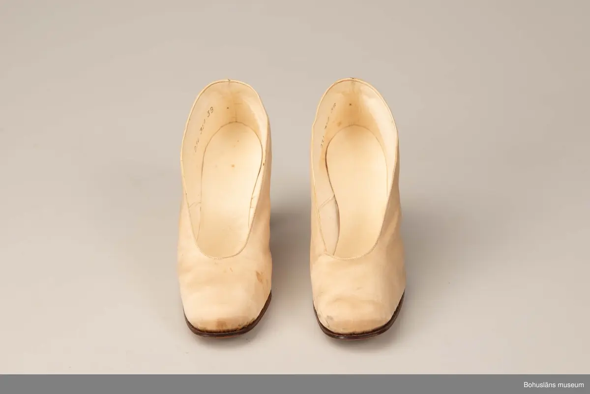 Högklackad damsko, utvändigt vitt siden, invändigt vitt skinn, lädersula. Pumps storlek 38.
Skrapmärken och missfärgningar. 
Greta Karlssons brudskor från år 1922.
Placerade i skolåda UM018555.

Se UM018527
Sammanhör med UM018591 Brudslöja, UM018595 Brudbukett och UM018596 Diadem.