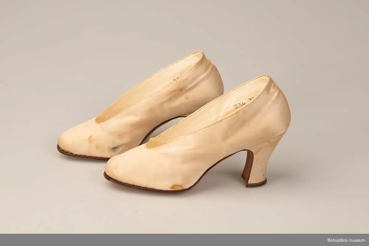 Högklackad damsko, utvändigt vitt siden, invändigt vitt skinn, lädersula. Pumps storlek 38.
Skrapmärken och missfärgningar. 
Greta Karlssons brudskor från år 1922.
Placerade i skolåda UM018555.

Se UM018527
Sammanhör med UM018591 Brudslöja, UM018595 Brudbukett och UM018596 Diadem.