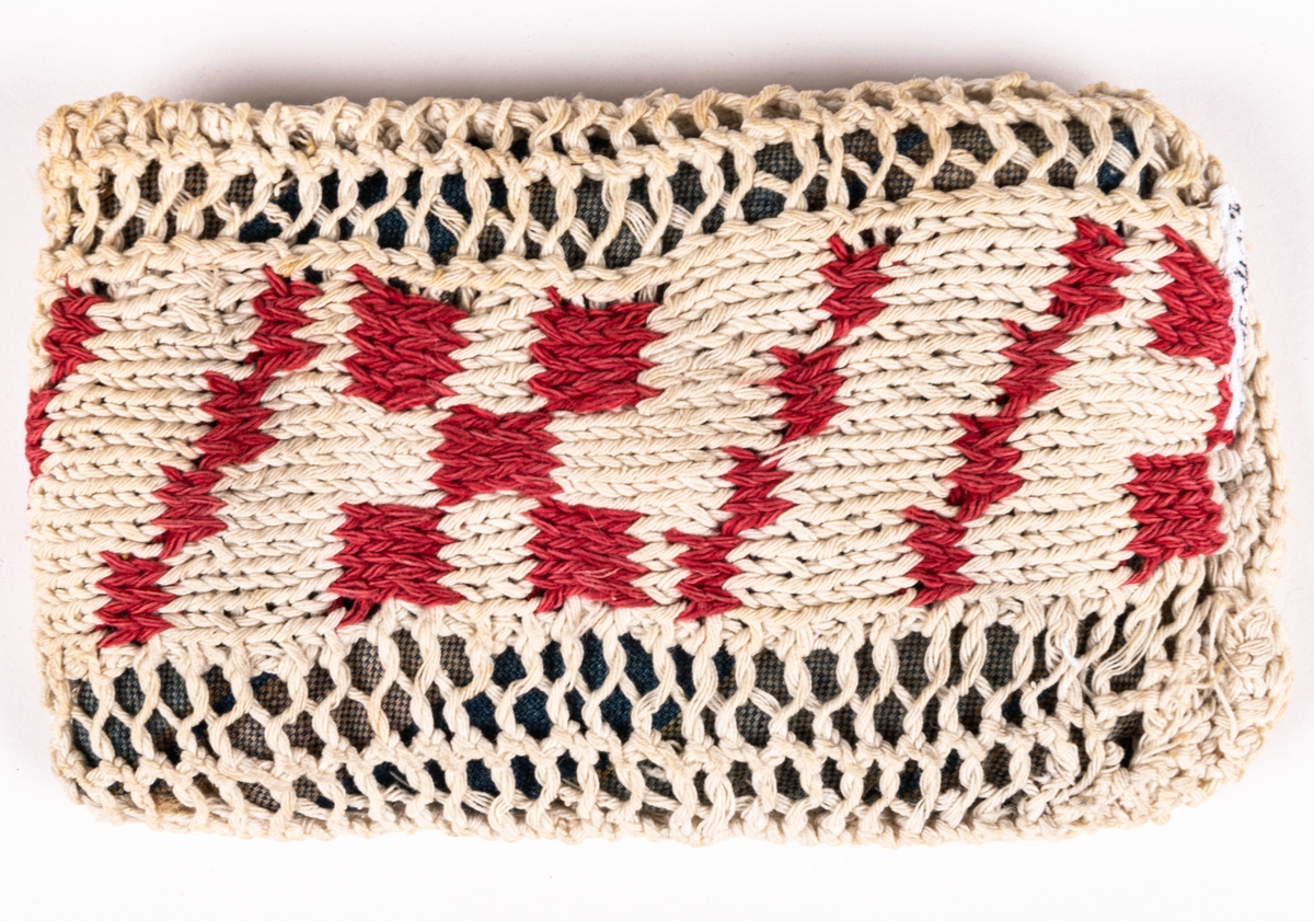 Dyna, till docka.
Stickad remsa med röda rutor. Hopsydd med flätsöm. Fylld innerdyna.
Mönsterstickad med vitt och rött bomullsgarn. Blåvitt bomullstyg och fyllning.