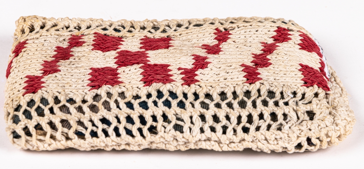 Dyna, till docka.
Stickad remsa med röda rutor. Hopsydd med flätsöm. Fylld innerdyna.
Mönsterstickad med vitt och rött bomullsgarn. Blåvitt bomullstyg och fyllning.