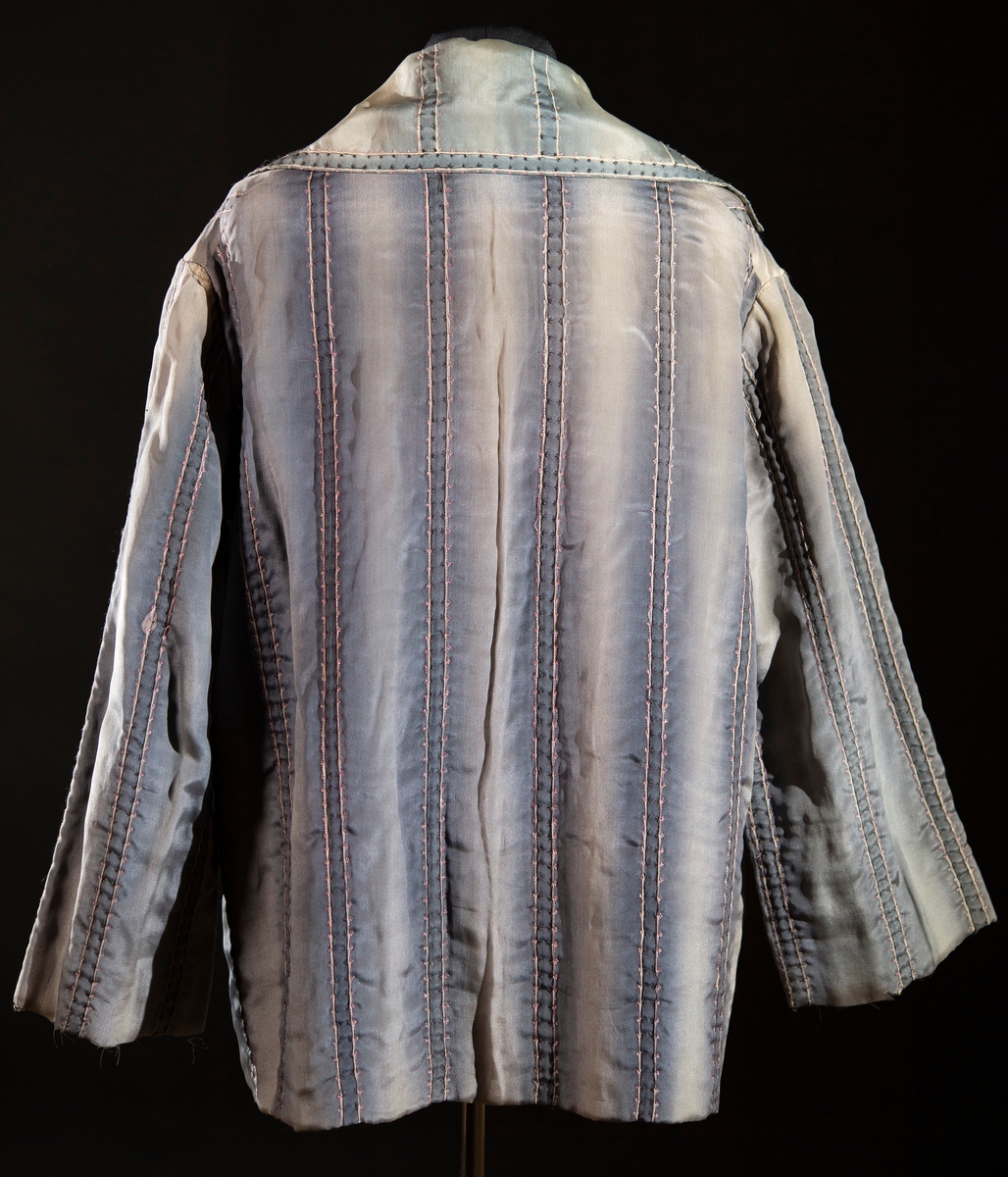 Av blågrått siden. Handbroderad med rosa och svart silke. Handtryckt sidenfoder med blom- och bladmotiv.