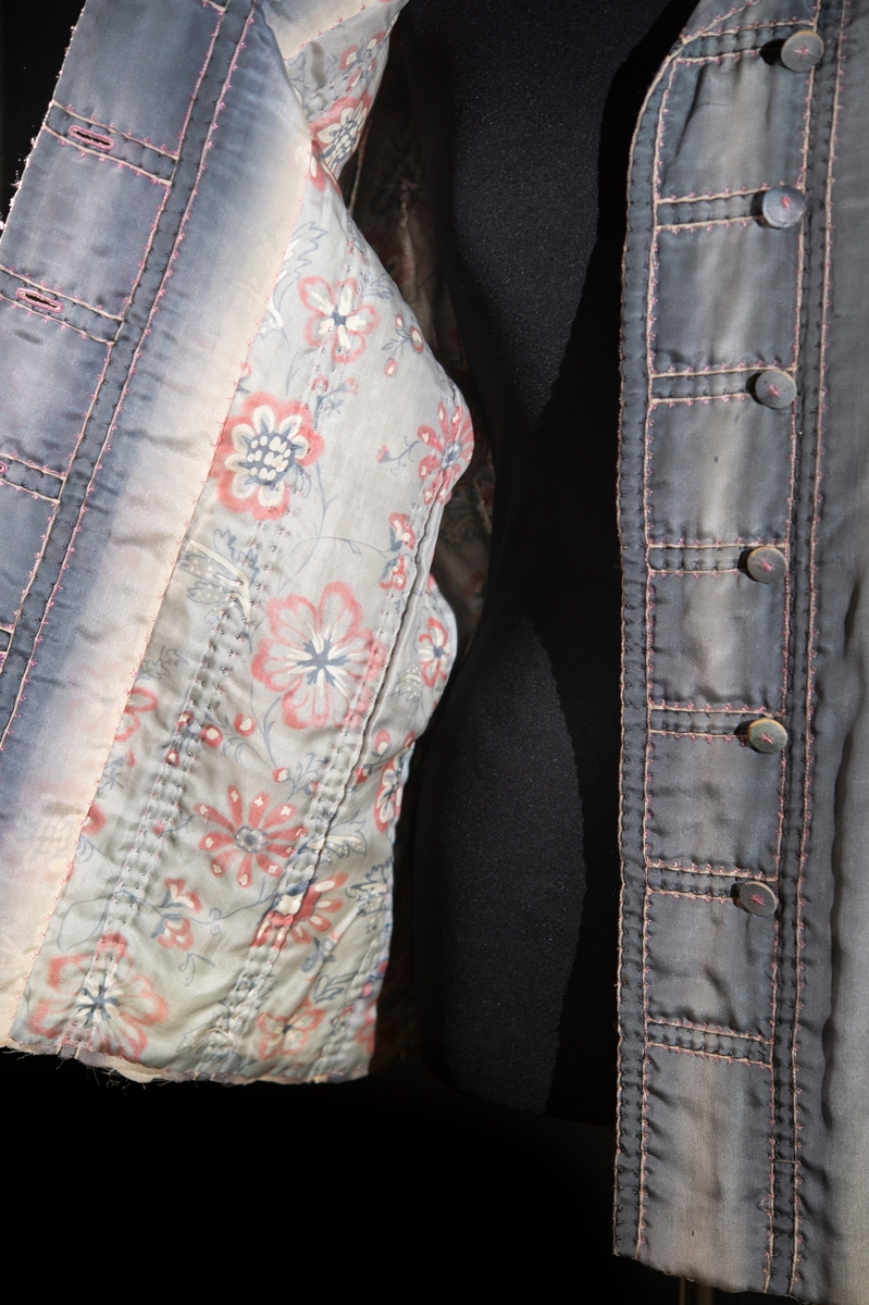 Av blågrått siden. Handbroderad med rosa och svart silke. Handtryckt sidenfoder med blom- och bladmotiv.